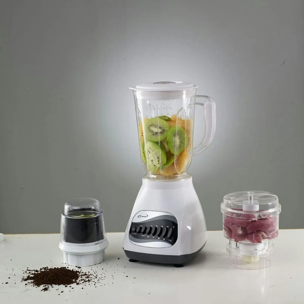 A countertop blender full of kiwi and other fruit, next to two small blender cups