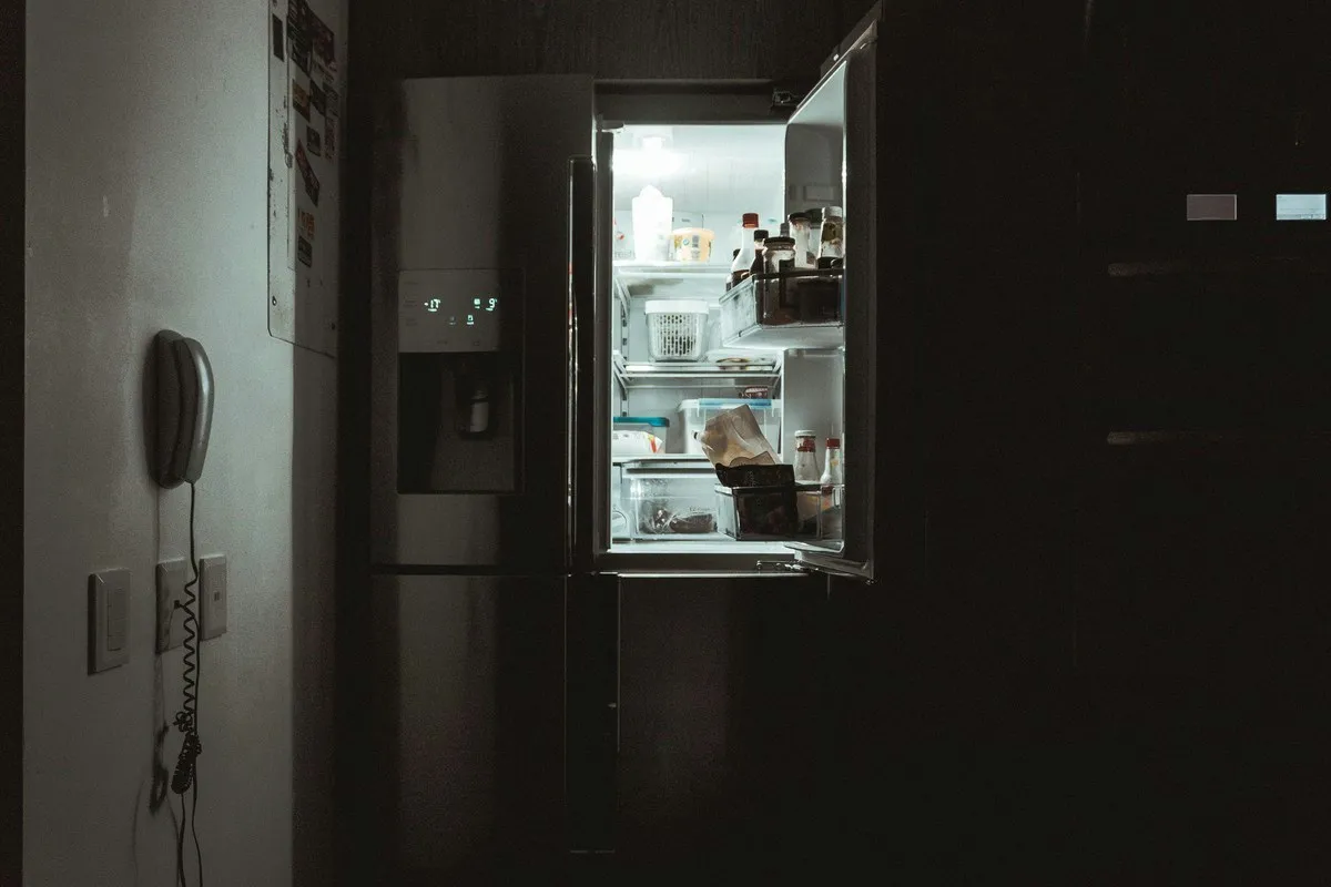 An open fridge glowing in a dark apartment kitchen