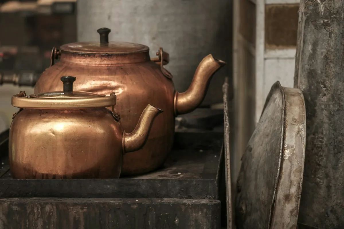 Two old copper stovetop kettles on a wooden shelf