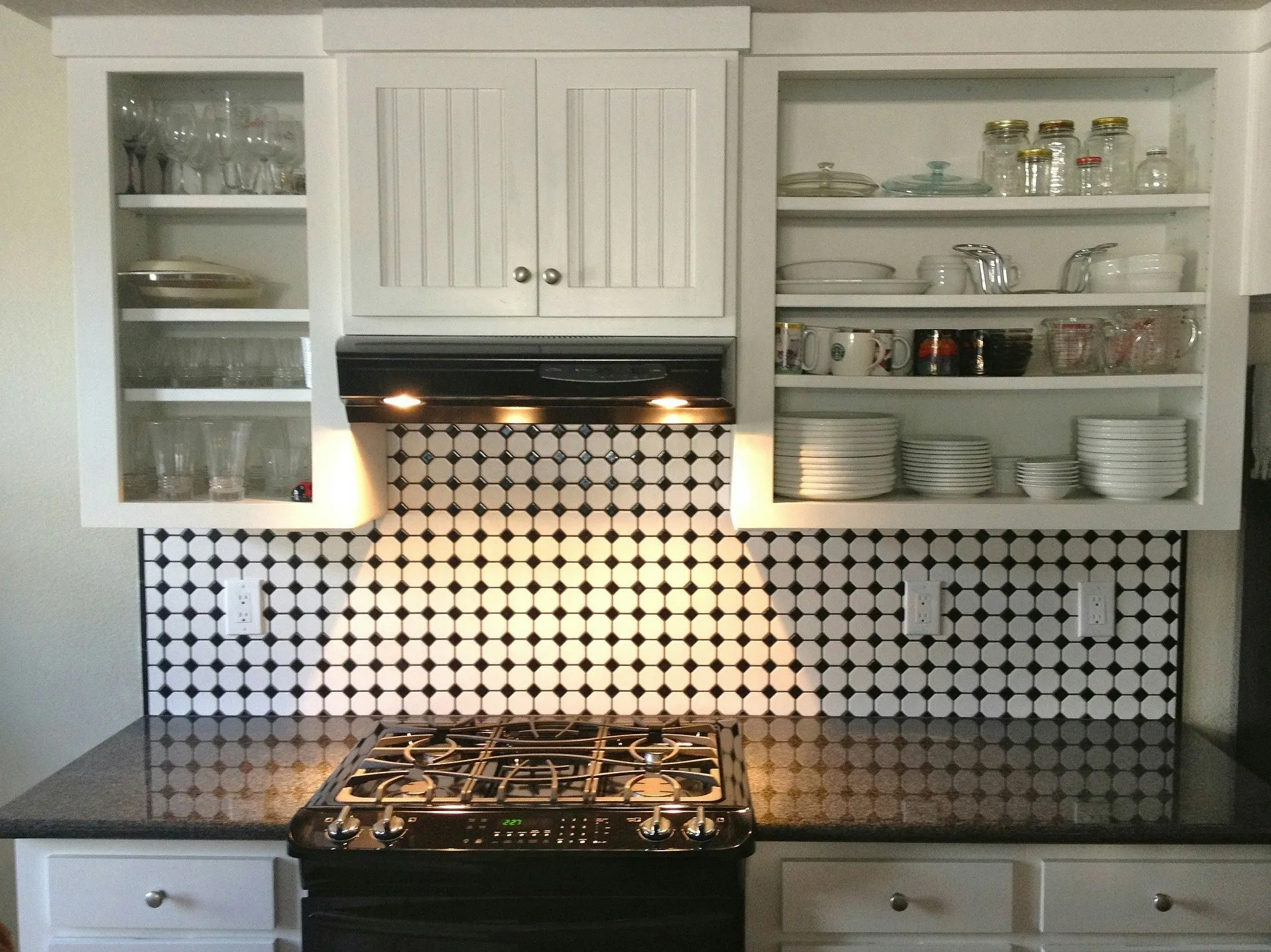 A gas cooktop under a range hood, with open shelves of dishes above