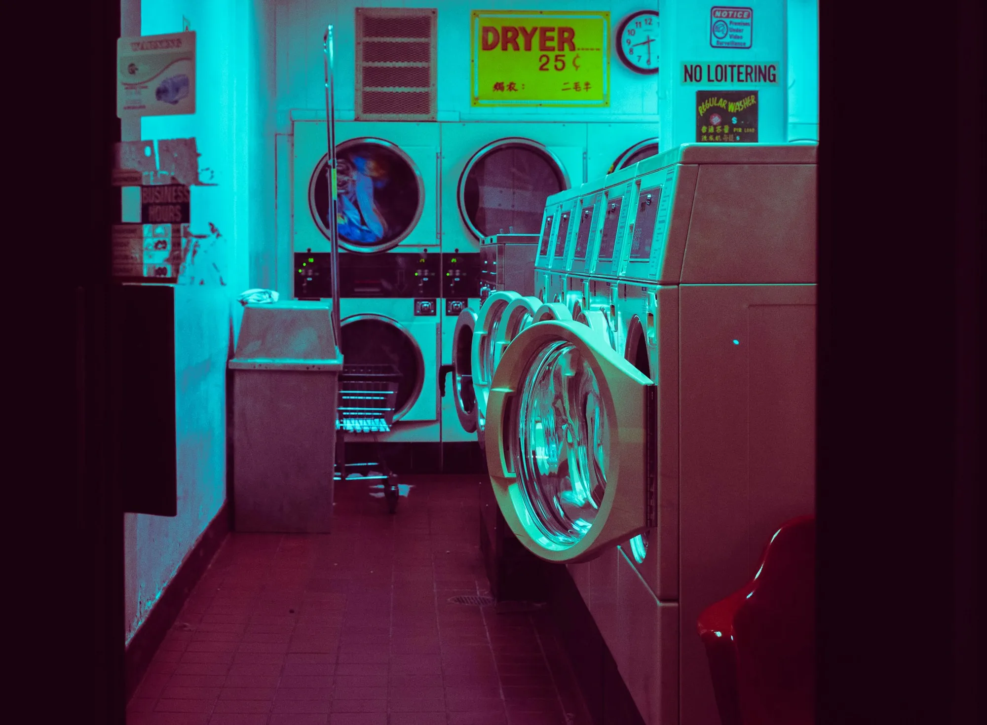 A row of washing machines in a laundromat lit in blue